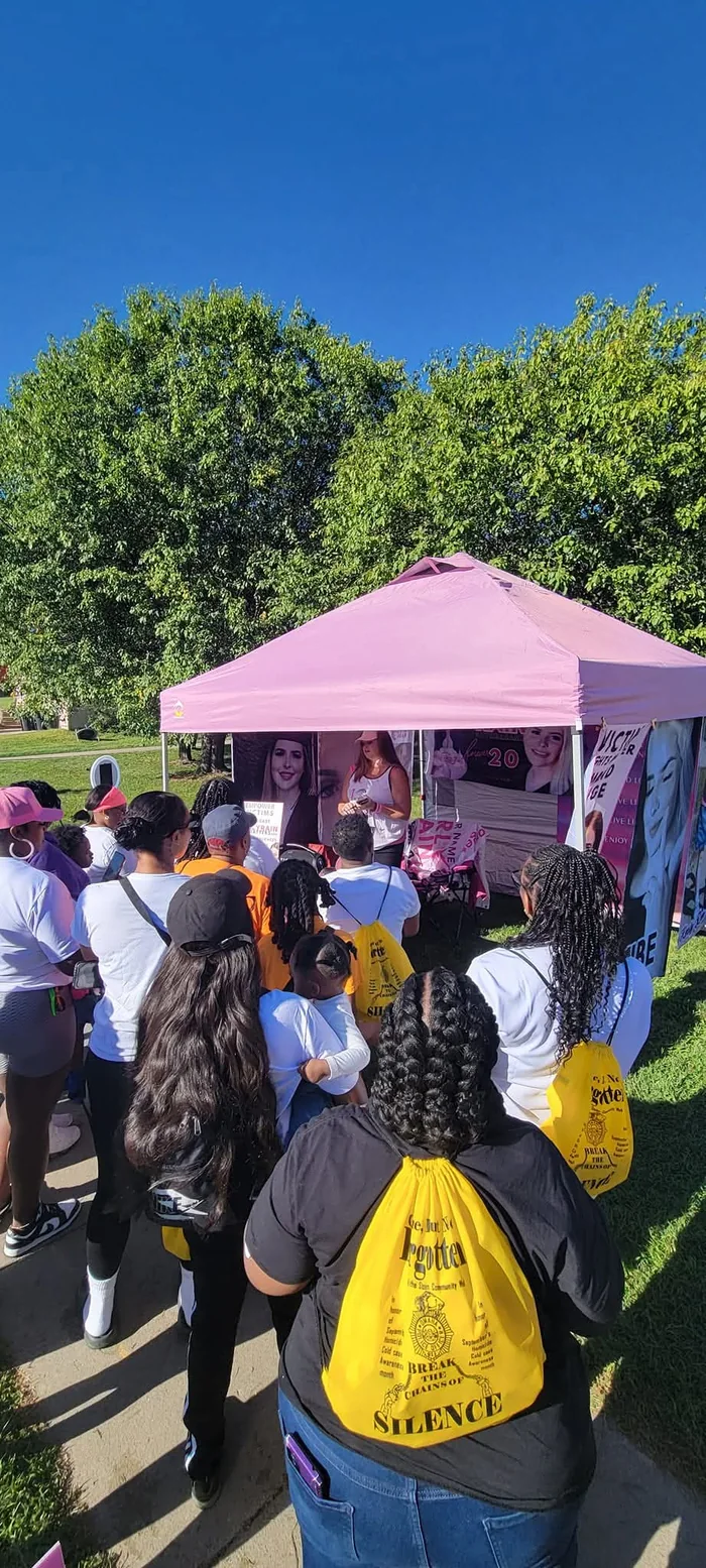 A crowd gathering at a pink tent covered with photos of Karly at a community walk.